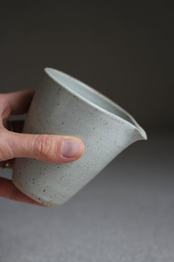 Hand hält kleines Milchkännchen mit kurzem Schnabel und ohne Henkel in Grau