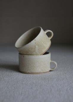 Zwei kleine Kaffeetassen in Beige mit Henkel ineinander gestellt