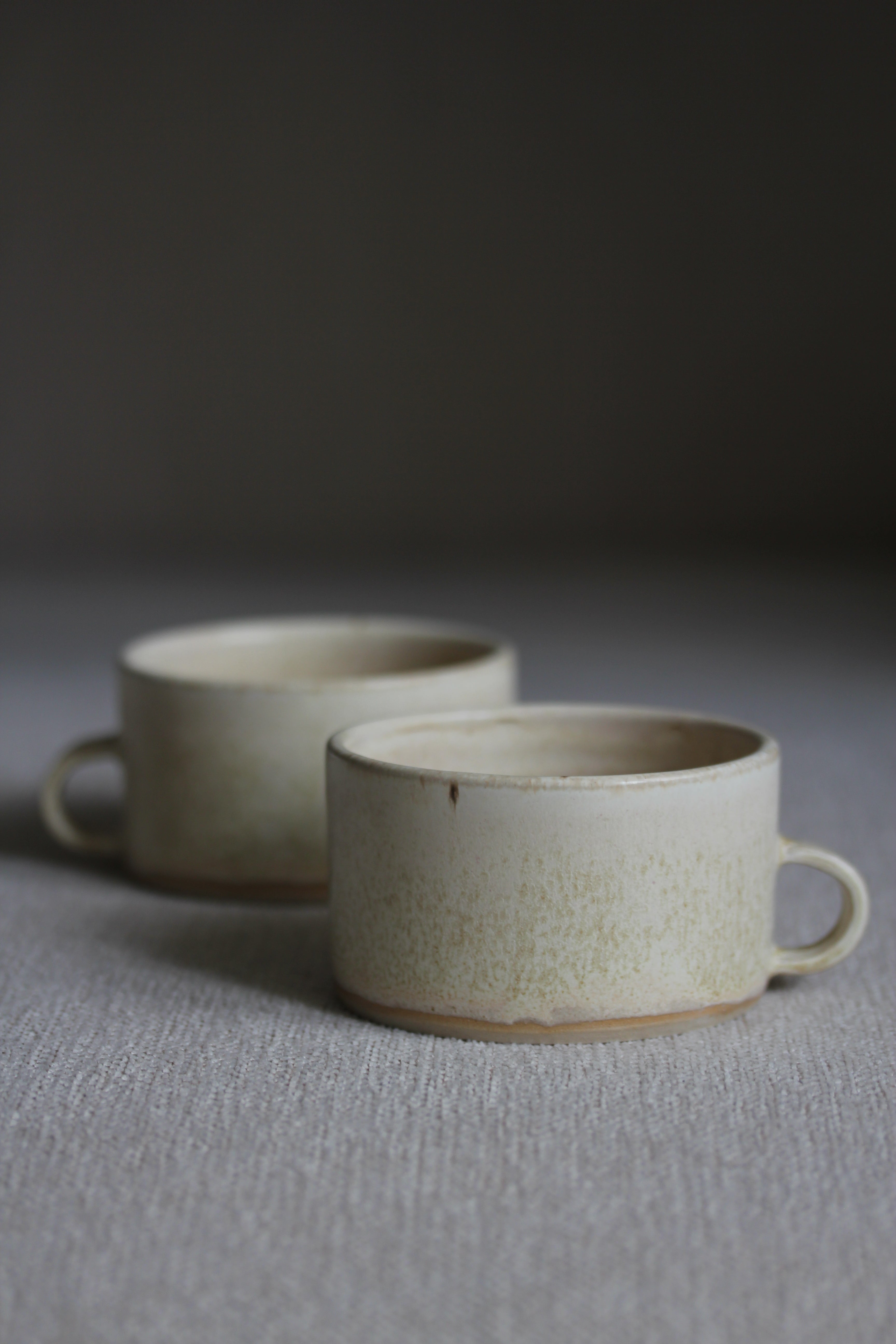 Zwei kleine Kaffeetassen in Beige mit Henkel nebeneinander stehend