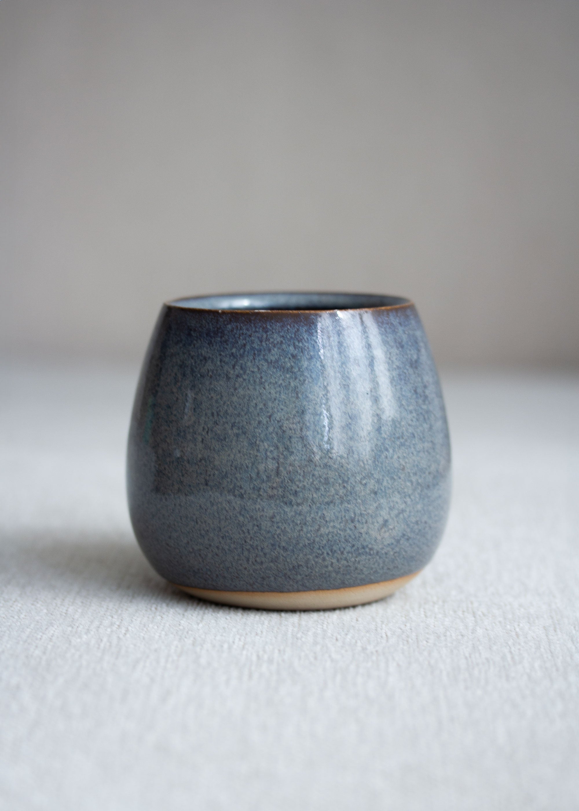 Runder, kleiner Blumentopf in Graublau mit kleinem braunen Rand an Boden und Öffnung