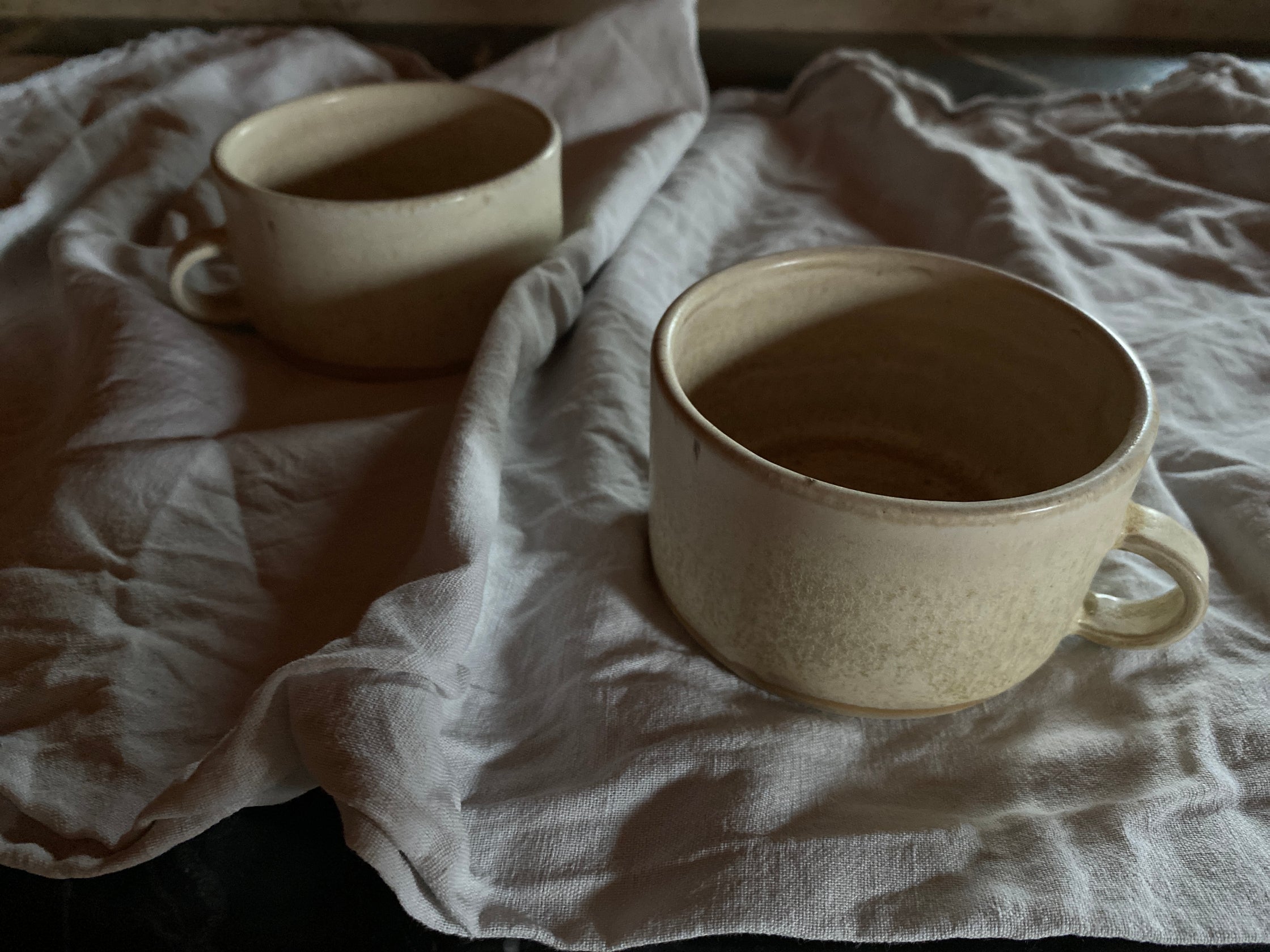 Zwei beige Kaffeetassen mit Henkel auf Tuch