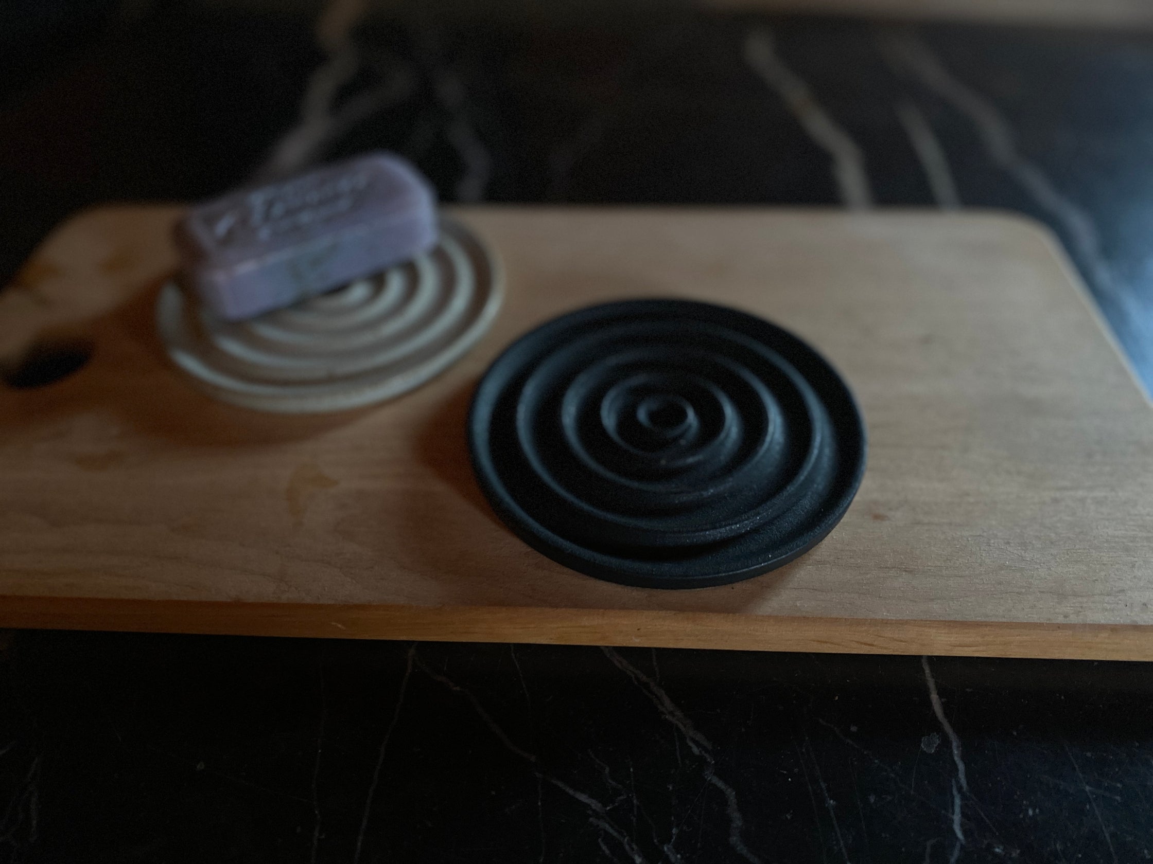 Eine schwarze und eine beige runde Seifenschale mit Seife auf Holzbrett